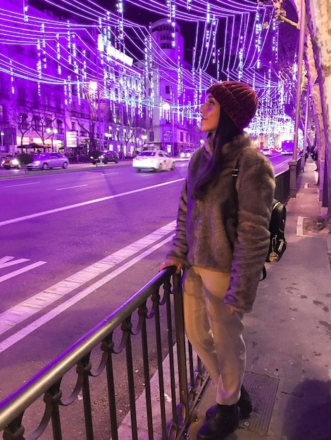 A traveler looking cautiously around a busy city street at night, with neon lights reflecting in puddles on the ground. The traveler is holding a map but appears unsure, capturing a sense of vulnerability.