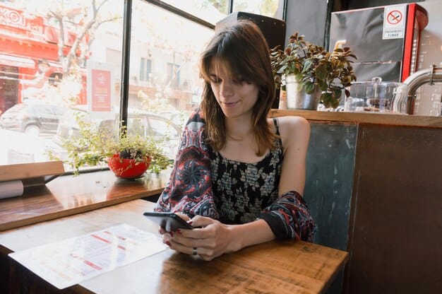 A person sitting at a cafe, using a translation app on their smartphone to communicate with a local waiter. The app displays text in both English and the local language.