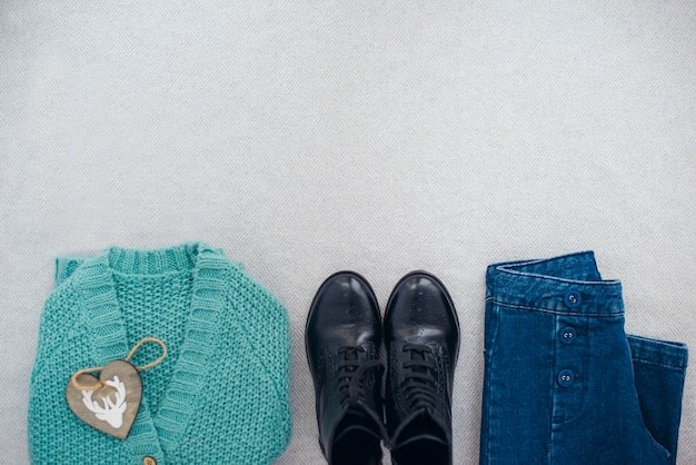 An overhead shot of a neatly arranged capsule wardrobe on a white surface. The wardrobe includes neutral-colored tops, bottoms, a dress, a cardigan, and versatile accessories like a scarf and belt.