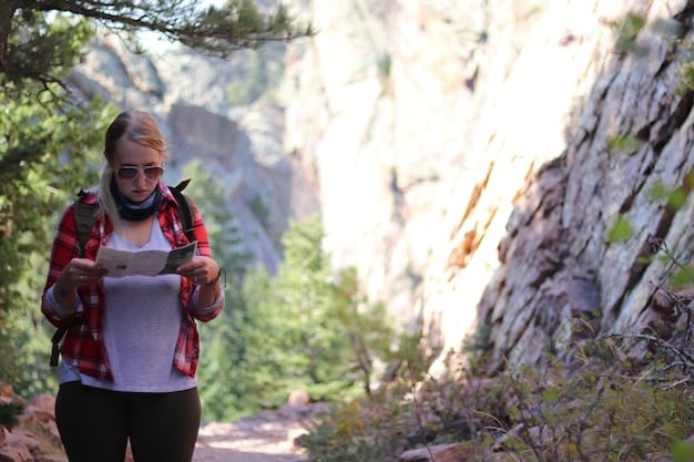 A hiker using a compass and topographic map in a mountainous area, with a GPS device visible on their wrist.