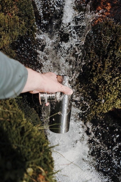 A hiker filling a reusable water bottle from a water fountain in a national park. The fountain has a sign encouraging water conservation.