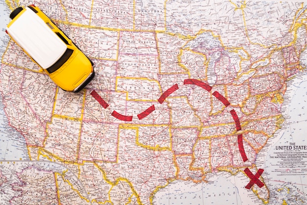 A close-up shot of a detailed road map highlighting a specific scenic route, with a compass and car keys resting on top. The map shows winding roads through mountainous terrain, indicating a challenging but rewarding drive.