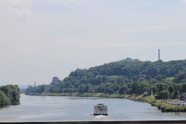 A panoramic vista of the Mississippi River, with a vintage steamboat cruising along the water. Lush green vegetation lines the banks, and a clear blue sky fills the background.