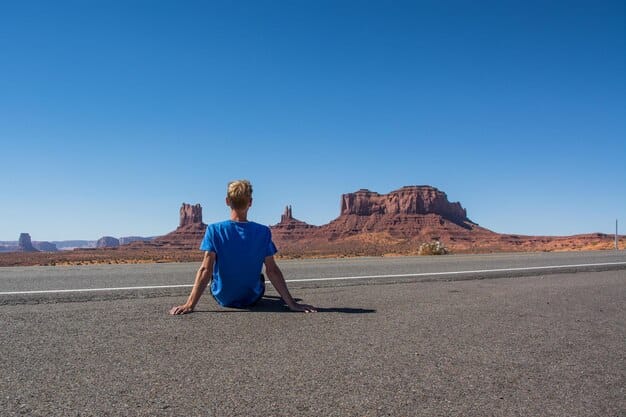 A panoramic view of Sedona, Arizona, with its distinctive red rock formations under a clear blue sky. A person is seen sitting in a meditative pose, overlooking the landscape.
