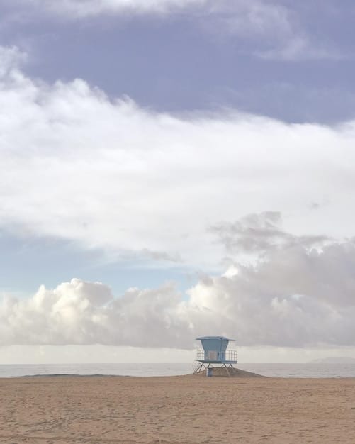 A scenic view of a nearly empty beach during the off-season. The sky is bright blue with a few fluffy clouds, and the ocean water is calm and clear. A family is strolling along the shoreline, enjoying the peace and quiet of the beach.