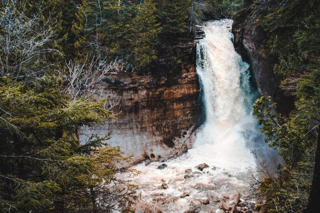 Brandywine Falls in Cuyahoga Valley National Park, Ohio. The waterfall is cascading down a rocky cliff, surrounded by lush greenery and trees. The image should capture the natural beauty and serenity of the scene.