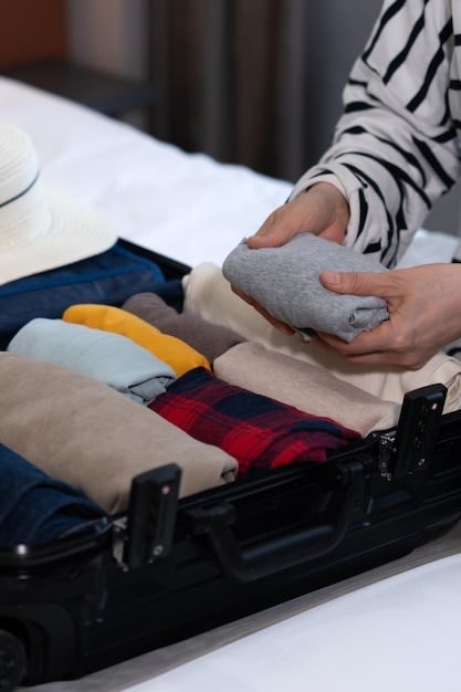 Close-up shot of hands carefully rolling a t-shirt, demonstrating the technique for maximizing space in a suitcase. The suitcase also contains other rolled garments and neatly organized items.